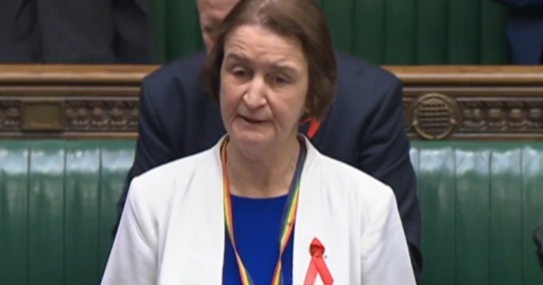 Labour MP Nia Griffith wearing a white suit jacket over a blue top, with a red ribbon for World AIDS Day, urges the government to ban conversion therapy while speaking in the House of Commons.