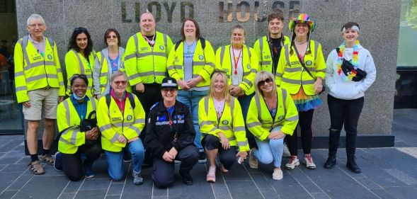 Members of the Birmingham StreetWatch crew wear yellow high-vis jackets, smiling in front of the police headquarters.