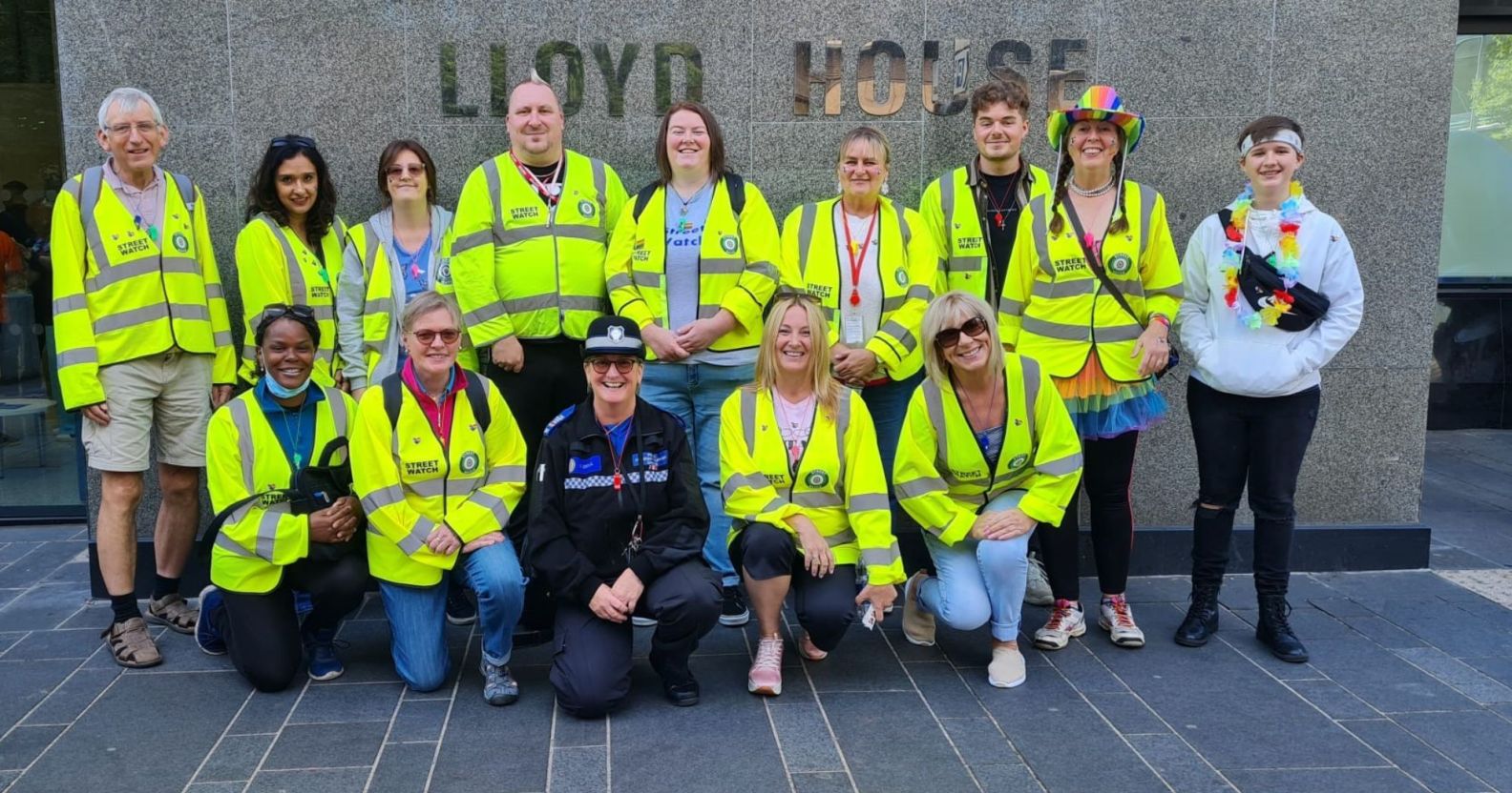 Members of the Birmingham StreetWatch crew wear yellow high-vis jackets, smiling in front of the police headquarters.