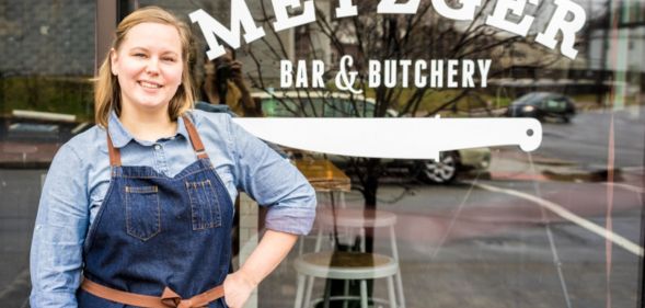 Metzger Bar and Butchery owner Brittanny Anderson stands outside her restaurant, wearing denim dungarees and a blue top.