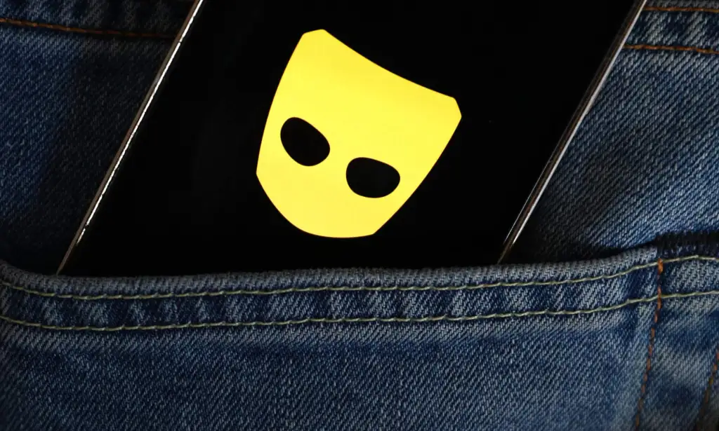 A mobile phone displays the yellow and black Grindr logo as the phone is tucked into the back pocket of a pair of jeans