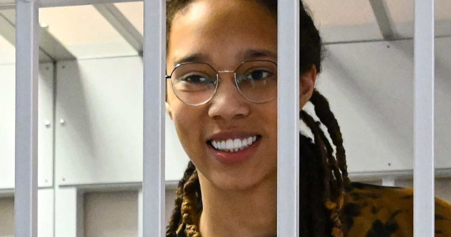 Brittney Griner smiles as she stands behind while bars while attending a Russian court hearing