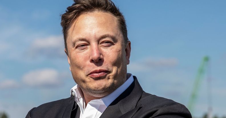 Elon Musk wears a white shirt and dark suit jacket as he stares somewhere off camera