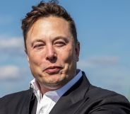 Elon Musk wears a white shirt and dark suit jacket as he stares somewhere off camera