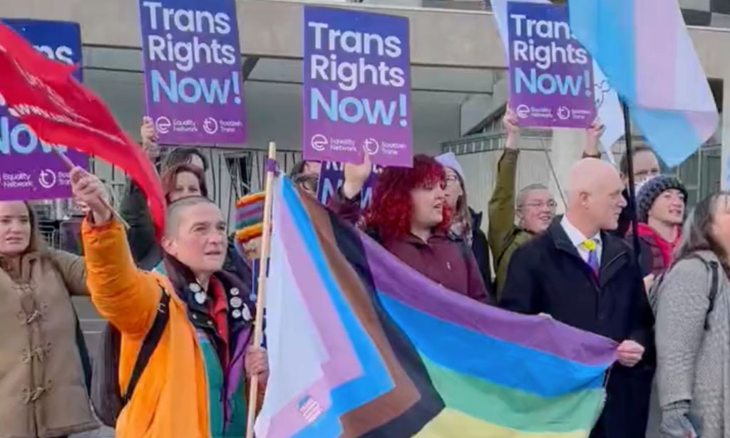 A group of people holding up the progressive Pride flag and signs in support of the trans community call on MSPs to pass the Gender Recognition Reform (Scotland) bill