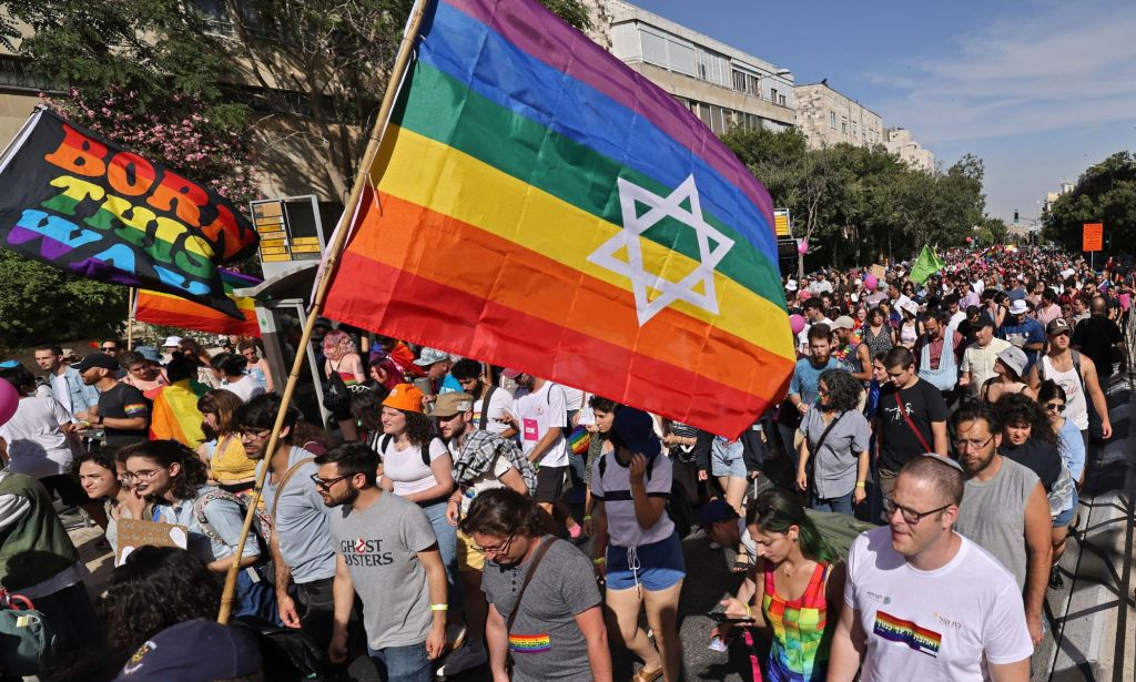 An Israeli flag, with the colours of the LGBTQ+ pride flag, waves above a crowd of people marching in a pride parade