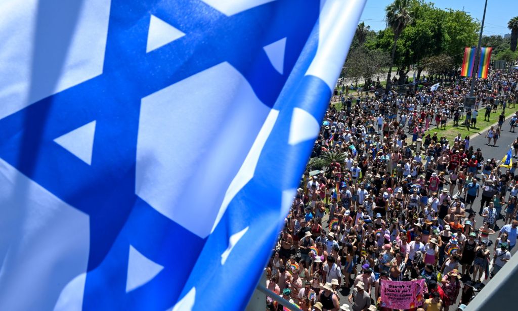 An Israeli flag frames thousands of people marching in the Tel Aviv Pride Parade in Jerusalem, Israel