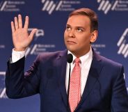 Republican politician George Santos gestures with his hands near his face while speaking at a podium