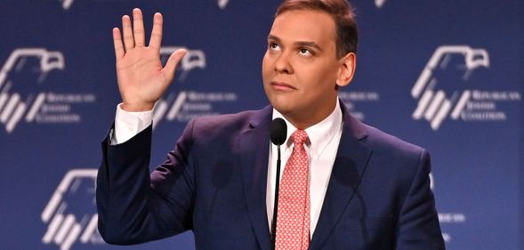 Republican politician George Santos gestures with his hands near his face while speaking at a podium
