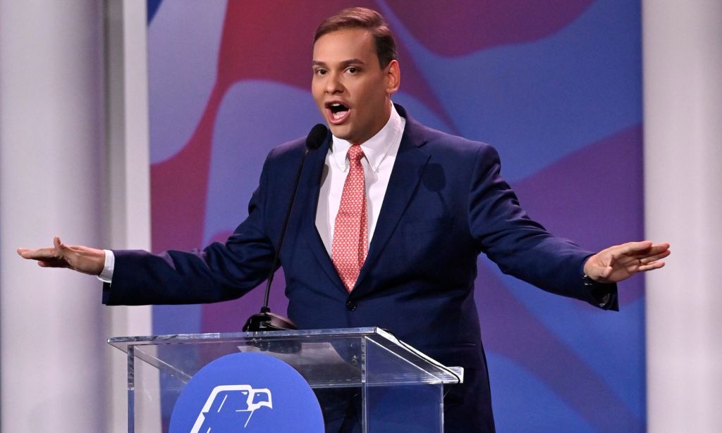 Republican politician George Santos gestures with his hands near his face while speaking at a podium