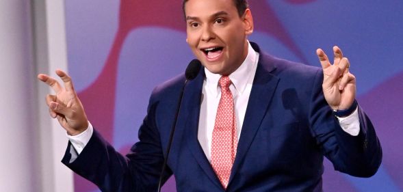Republican politician George Santos gestures with his hands near his face while speaking at a podium