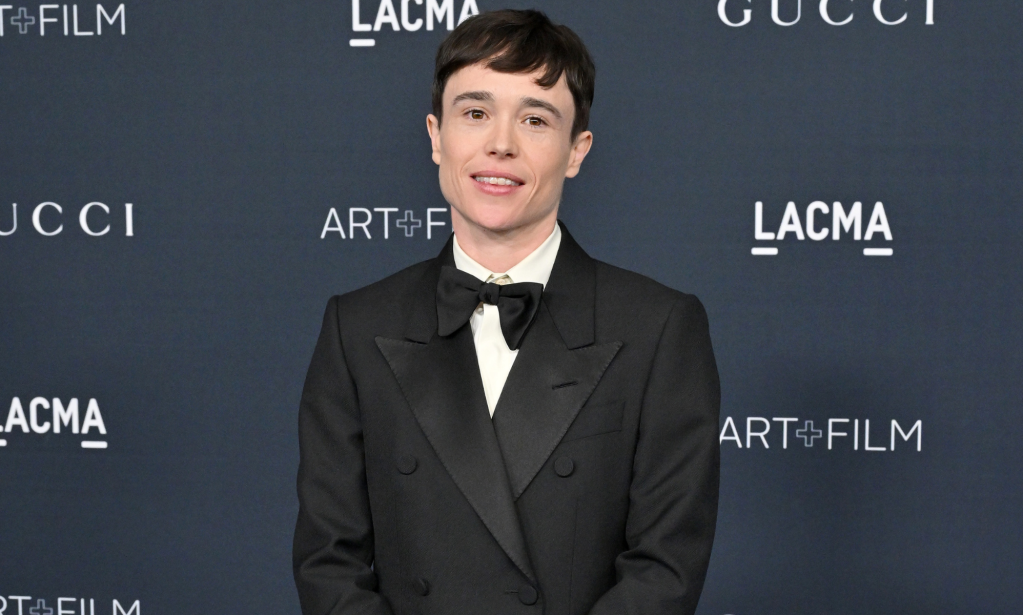 Elliot Page smiles at the camera while wearing a black and white tuxedo