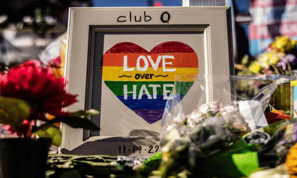 Flowers and a picture of a heart drawn in Pride rainbow colours with the message "Love over Hate" are placed outside Club Q