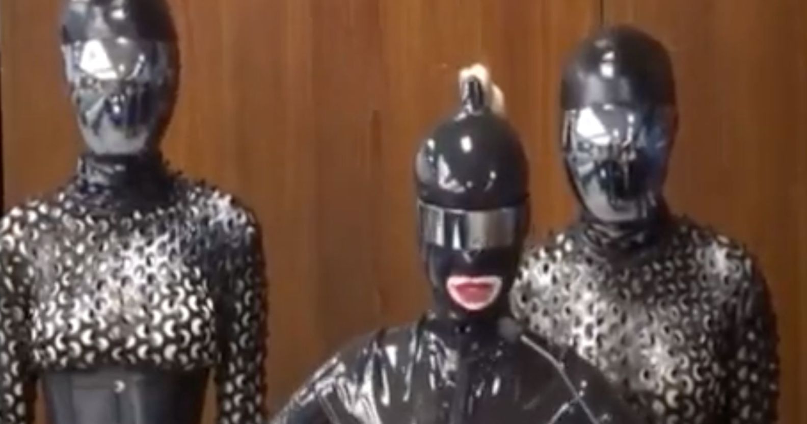 A screengrab from Twitter shows three people dressed in black latex, head-to-toe body suits standing in front of a wall