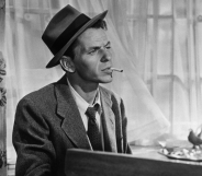 Black and White photo of Frank Sinatra sitting at a piano smoking a cigarette wearing a suit and tie.