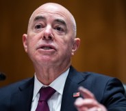 Alejandro Mayorkas wears a black suit with burgendy tie, while speaking at the Senate building in a Homeland Security meeting.