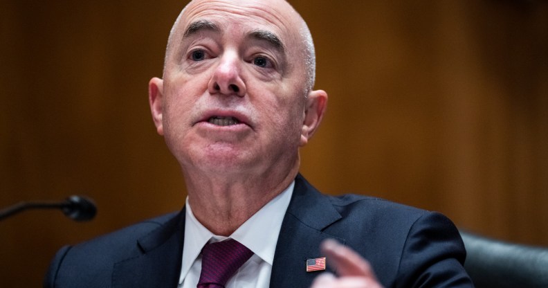 Alejandro Mayorkas wears a black suit with burgendy tie, while speaking at the Senate building in a Homeland Security meeting.