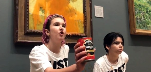 A photo of Just Stop Oil activists Anna Holland and Phoebe Plummer wearing T-shirts with the slogan "Just Stop Oil" kneel in front of Van Gogh's Sunflowers in London's National Gallery, which is covered in tomato soup