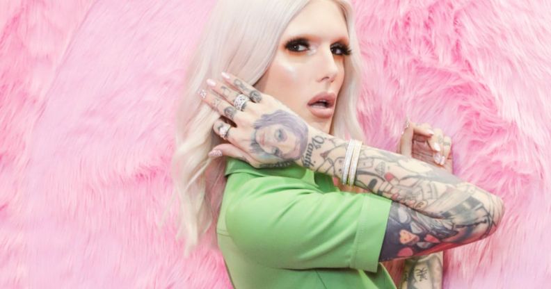 Jeffree Star wearing a green suit and sporting long blonde hair standing against a pink background.