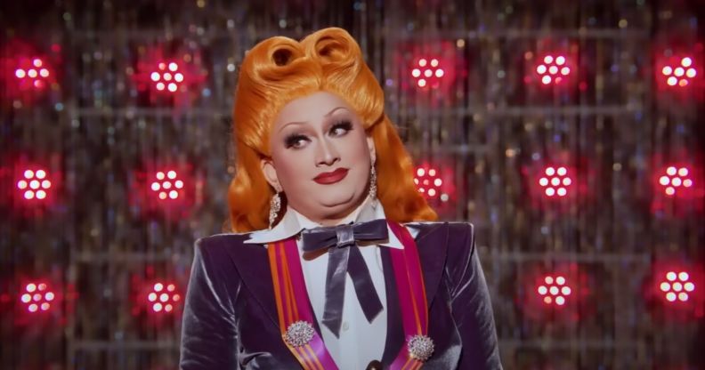 A stil from Drag Race All Stars 7 showing drag queen inkx Monsoon in a white and purple outfit and orange wig