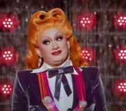 A stil from Drag Race All Stars 7 showing drag queen inkx Monsoon in a white and purple outfit and orange wig
