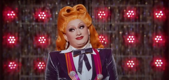 A stil from Drag Race All Stars 7 showing drag queen inkx Monsoon in a white and purple outfit and orange wig