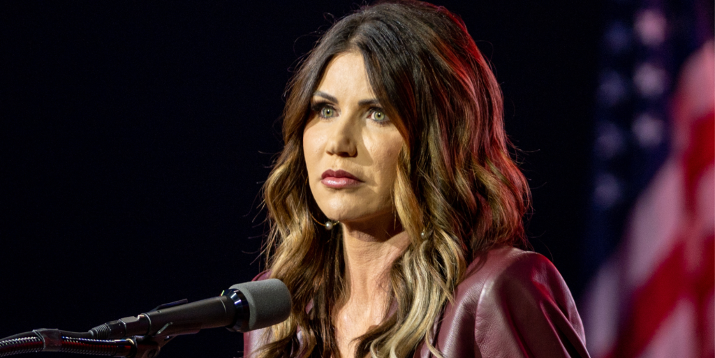 A photo shows South Dakota's republican governor Kristi Noem standing behind a microphone with the American flag can be seen in the background