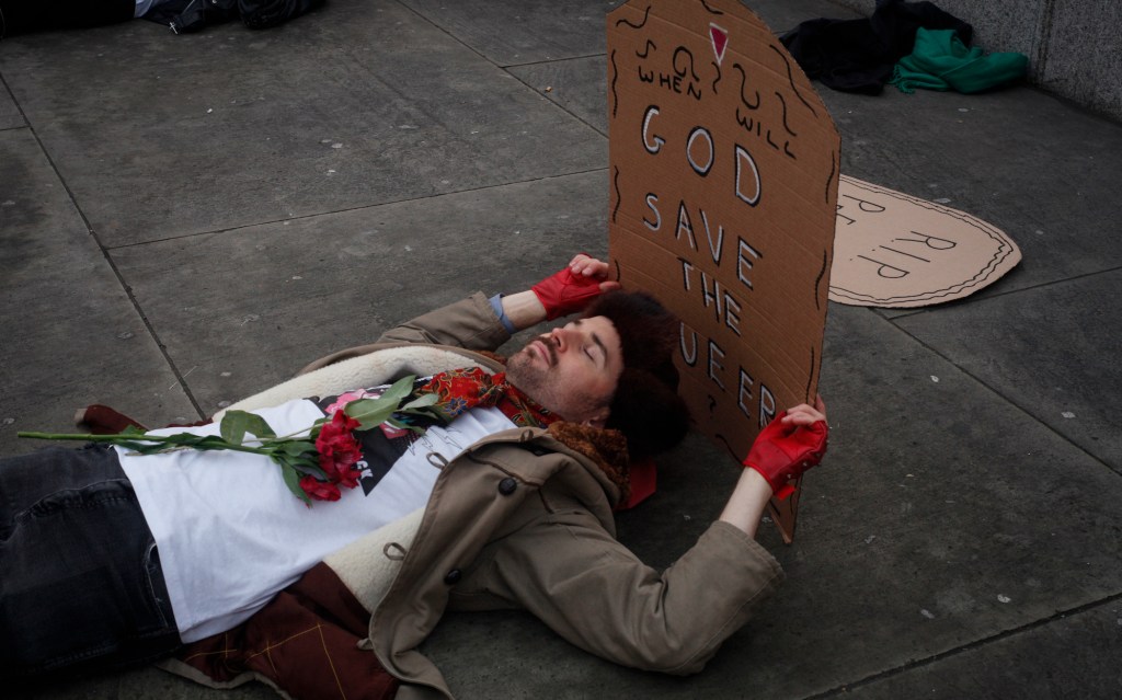 An activist holds a sign which reads: "God save the queer"