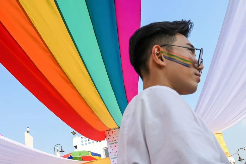 A member of the LGBTQ+ community stands under a rainbow flag displayed on a boat during the Pride Boat Parade, an event of the Myanmar's Yangon Pride festival in Yangon.