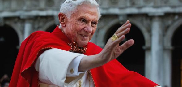 Pope Benedict XVI pictured during his reign wearing white and red robes and raising his hand in a wave to adoring crowds.