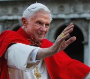 Pope Benedict XVI pictured during his reign wearing white and red robes and raising his hand in a wave to adoring crowds.