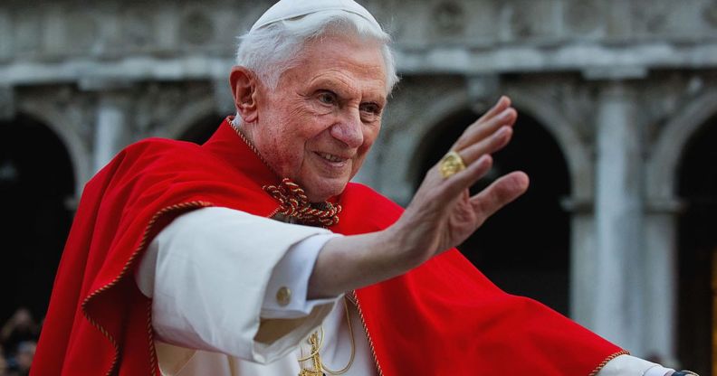 Pope Benedict XVI pictured during his reign wearing white and red robes and raising his hand in a wave to adoring crowds.