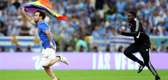 A photo of a pitch invader wearing a shirt reading "Save Ukraine" as he holds a rainbow flag during the FIFA World Cup Qatar 2022.
