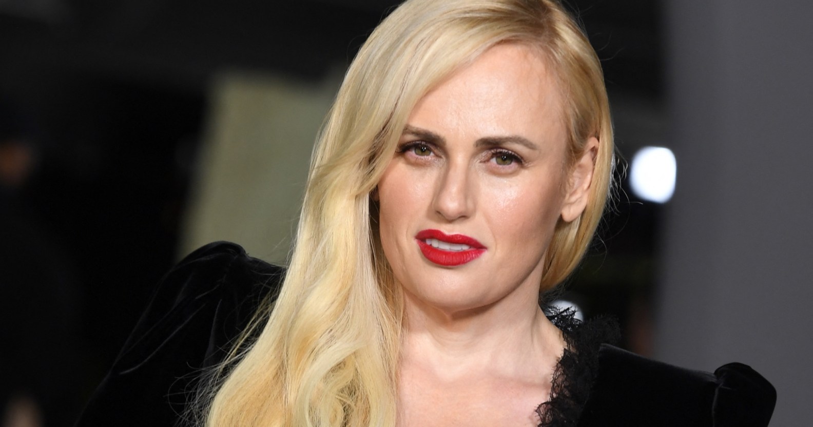 Rebel Wilson slightly tilted wearing red lipstick and a black dress, cropped to show her shoulder and head (Getty)