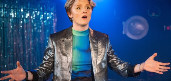 A photo of actor Rosanna Suppa wearing a silver waistcoat over a neon blue top performing on stage as Sue Albright in Lesbian Space Crime. (Cam Harle real)