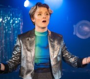 A photo of actor Rosanna Suppa wearing a silver waistcoat over a neon blue top performing on stage as Sue Albright in Lesbian Space Crime. (Cam Harle real)