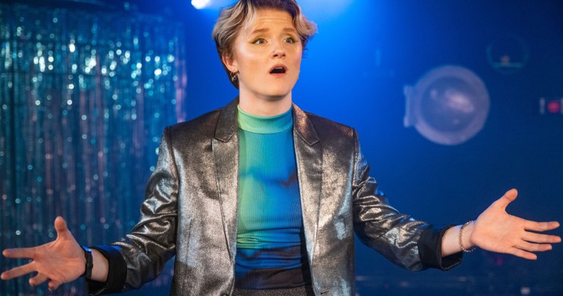 A photo of actor Rosanna Suppa wearing a silver waistcoat over a neon blue top performing on stage as Sue Albright in Lesbian Space Crime. (Cam Harle real)