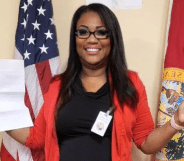 Florida Republican Lavern Spicer wearing a black top and red cardigan stands in front of an American flag