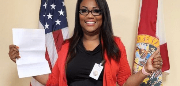Florida Republican Lavern Spicer wearing a black top and red cardigan stands in front of an American flag