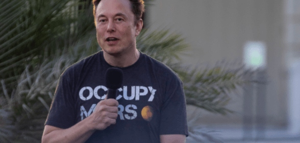Elon Musk stands with a microphone, wearing an "occupy Mars" T-shirt