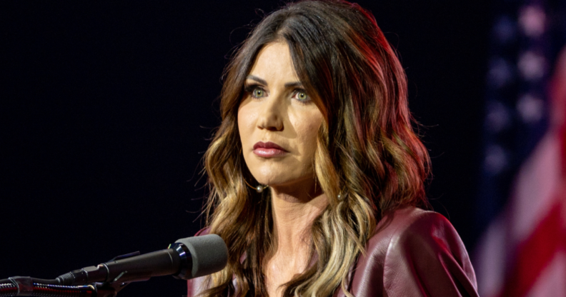 A photo shows South Dakota's republican governor Kristi Noem standing behind a microphone with the American flag can be seen in the background