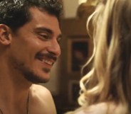 A still from The White Lotus showing actor Stefano Gianino as Niccolo smiling as he strips down in front of a woman with blonde hair who is turned away from the camera