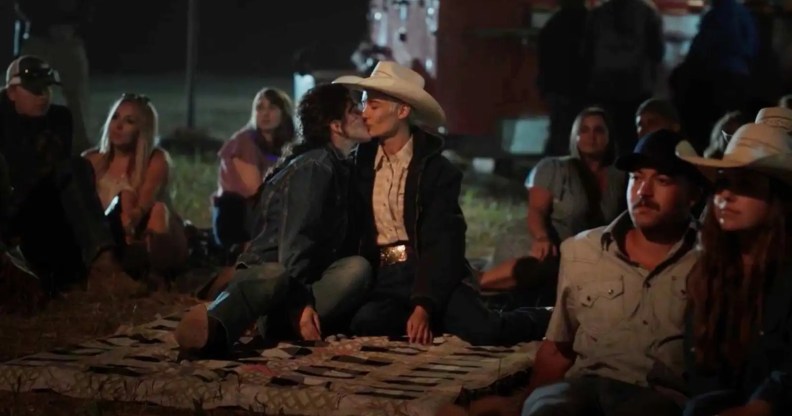 Still from TV series Yellowstone showing actor Lilli Kay as Clara wearing a denim jacket and jeans kissing a woman wearing a black coat, white shirt and white cowboy hat