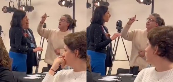 A woman screams and points at the back of a room of people sitting at tables, who appear very uncomfortable