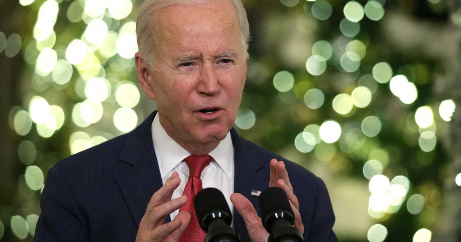 Joe Biden speaking into a microphone, there are Christmas trees in the background