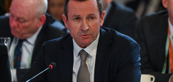 Western Australia Premier Mark McGowan dressed in a dark suit, white shirt and grey tie sits in front of a microphone
