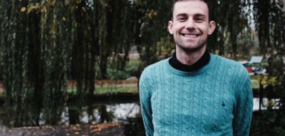 Photo of Christian teacher Joshua Sutcliffe wearing a turquoise top smiling as he stands in a countryside setting