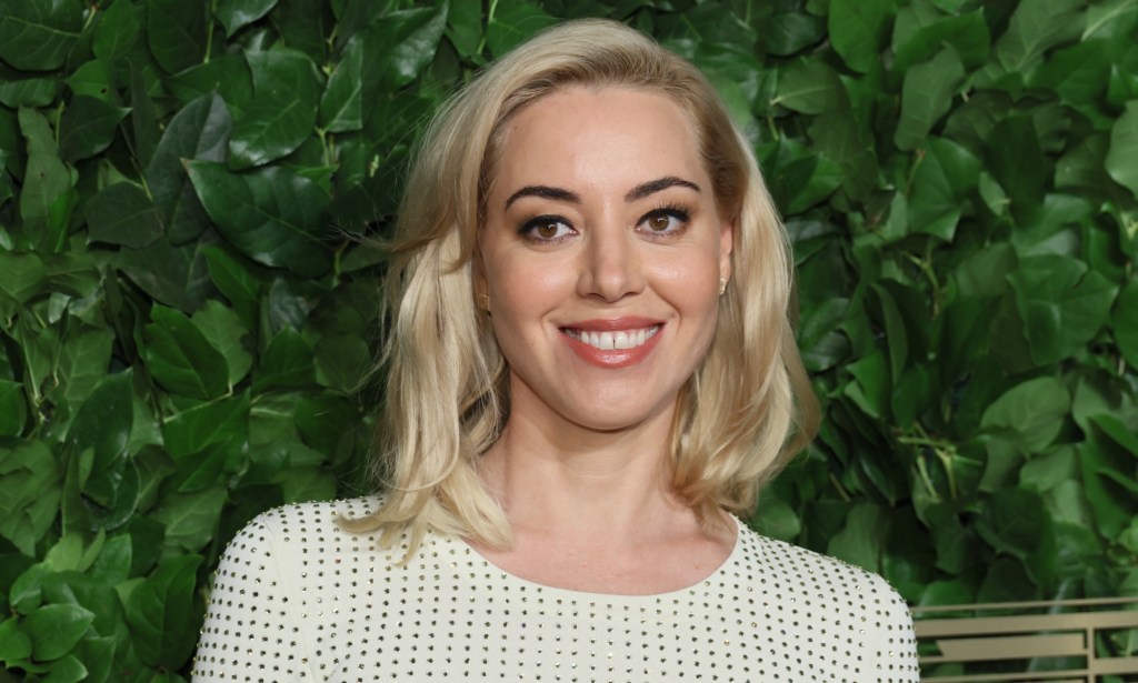 Aubrey Plaza smiling as she wears white and black dotted top.