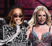 An image shows singer dressed in an elaborate black and white outfit as she sings into a microphone with Britney Spears positioned next to the wearing a burlesque-style outfit. (Getty)
