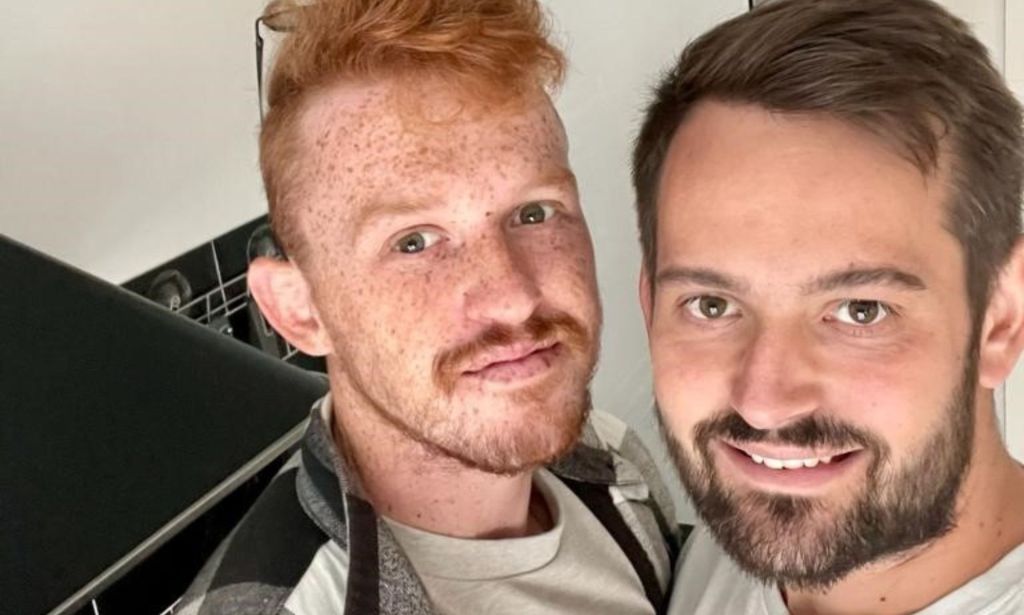 Ricardo and Bradleigh, a gay couple from Essex, wear white shirts and plaid shirts on top as they smile at the camera for a selfie